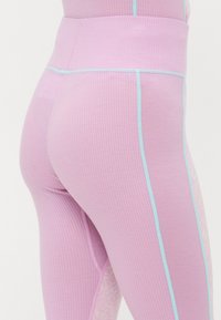 Rosa ribbade leggings med ljusblå accenter längs sömmarna och ett mönster av spetspanel på sidan. Midjan är bred för stöd.