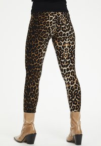 Leggingi s uzorkom leopard su crne boje s zlatnim i smeškim mrljama. Tkanina je rastezljiva, što dodatno naglašava uski kroj.
