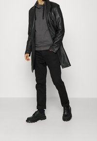 Manteau en cuir noir sur un sweat à capuche gris, associé à un pantalon noir et des chaussures noires massives. Tenue décontractée en couches avec un design épuré.