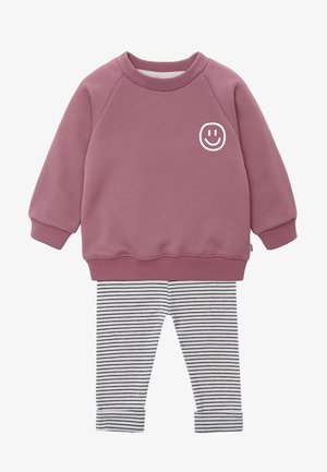 Rosa Sweatshirt mit einem weißen Smiley-Gesicht-Design, kombiniert mit schwarzen und weißen gestreiften Leggings. Weicher Stoff mit gerippten Bündchen und Hüftbund.