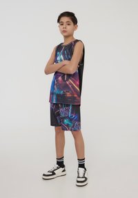 Completo canotta e pantaloni shorts per ragazzi in nero con grafiche neon vivaci. Presenta una vestibilità ampia, design senza maniche e motivi a contrasto.