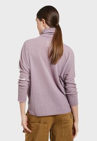 Fioletowy sweter dzianinowy z wysokim kołnierzem, rękawami 3/4 i prążkowaną fakturą; noszony z beżowymi spodniami cargo. Tylny widok ukazuje luźny krój.