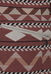 Textil med ett geometriskt mönster av diamanter och zickzackar i nyanser av vinröd, beige och svart, med en liten detalj av dragkedjeficka.