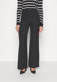 Czarne spodnie z wysokim stanem wykonane z gładkiego materiału, z rozszerzanym krojem nogawki. W zestawie z czarną i białą, paskowaną bluzką z długim rękawem.