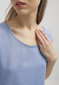 Vaaleansininen, lyhythihainen paita, joka on valmistettu pehmeästä kankaasta. Ominaisuuksiin kuuluu pyöreä pääntie ja sileä pinta, yksinkertainen ja koristelematon muotoilu.