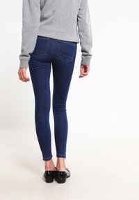 Jeans ajustados en denim azul oscuro, con un diseño de tiro medio, bolsillos traseros minimalistas y una silueta ajustada, llevados con zapatos planos negros.