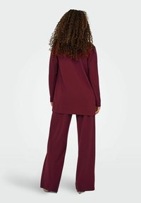 Tunique longue bordeaux à manches longues associée à un pantalon ample, fabriquée dans un tissu lisse. Offre une coupe décontractée et un ourlet droit pour le confort.
