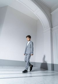 Szary garnitur o slim fit, z jednorzędową marynarką, w połączeniu z białą koszulą i czarnymi butami, na marmurowej podłodze.