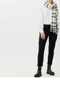 Camisa blanca de botones con mangas fruncidas, pantalones negros, botas cortas negras y una bufanda a cuadros gris con flecos.