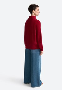 Roter, gerippter Rollkragenpullover, lässige Passform, kombiniert mit weit geschnittenen blauen Jeans, die einen rohen Saum und minimale Details aufweisen.