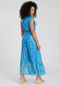 Robe maxi en tissu léger bleu clair avec un motif floral, manches volantées, ourlet à volants, associée à des sandales compensées beiges.