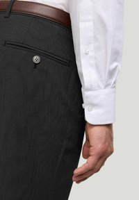 Graue, strukturierte Hosen mit einer Gesäßtasche und einem Knopf. Ein weißes Langarmhemd mit geknöpften Manschetten ist sichtbar, zusammen mit einem braunen Gürtel.