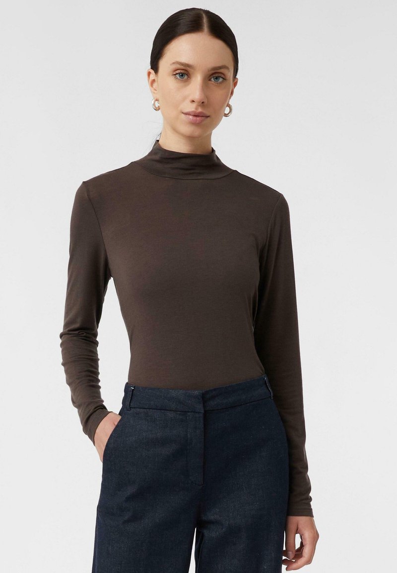 Brauner Langarm-Turtleneck-Shirt aus weichem Stoff, kombiniert mit dunkelblauen, maßgeschneiderten Hosen mit einer Fronttasche.