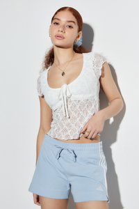Witte kanten crop top met korte gerimpelde mouwen en een strik aan de voorkant. Lichtblauwe sportieve shorts met witte zijstrips, elastische tailleband en logo.