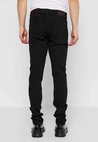 Jeans de mezclilla negra con corte ajustado, costuras visibles y dos bolsillos traseros. Llevados con botas negras hasta el tobillo. Etiquetados con "ONLY & SONS."