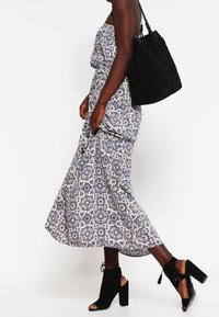 Kvinna klädd i en utan axelband mönstrad maxiklänning, svarta peep-toe klackar med blocktå, och bär en stor svart axelväska.