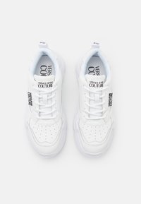 Baskets blanches avec des détails perforés, languette rembourrée et lacets. Présente le logo "VERSACE JEANS COUTURE" sur le côté. Semelle en caoutchouc.