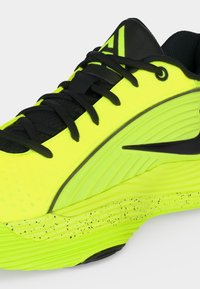 Chaussure de sport jaune néon et noire avec lacets noirs, semelle intermédiaire tachetée et panneau latéral texturé.
