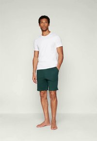 Witte korte mouwen t-shirt, gecombineerd met donkergroene shorts. De outfit heeft een eenvoudig ontwerp met een ontspannen pasvorm en een zachte textuur.