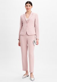 Lichtroest pak met een getailleerde blazer en rechte broekspijpen. Glad stof met een subtiele textuur. Zilveren ballerina's en een kleine metallic clutch.