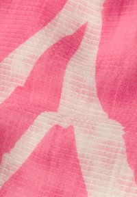 Gros plan sur un tissu texturé rose et blanc avec un motif abstrait ondulé et des fils tissés visibles.