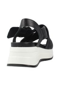 Sandalo in pelle nera con un design a fascia larga, dotato di una suola spessa bianca e un retro testurizzato nero. Dettaglio con cinturino regolabile alla caviglia.