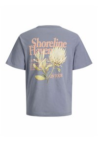 Šedé tričko s veľkým krémovým kvetom a zelenými listami, obsahujúce text "Shoreline Haven" a "On Tour" v broskyňovej farbe na zadnej strane.