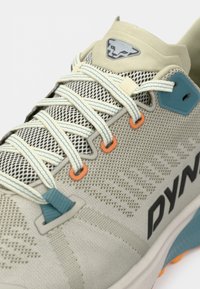 Αθλητικά παπούτσια σε ανοιχτό γκρι χρώμα με επάνω μέρος από διχτυωτό ύφασμα, μπλε και πορτοκαλί λεπτομέρειες και έντονο μαύρο λογότυπο. Διαθέτουν επίπεδα κορδόνια και υφή επιφάνειας.