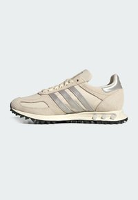 Μπεζ αθλητικό παπούτσι με συνδυασμό σουέτ και συνθετικών υλικών. Τρεις μεταλλικές ασημί ρίγες και ανθεκτική μαύρη σόλα.