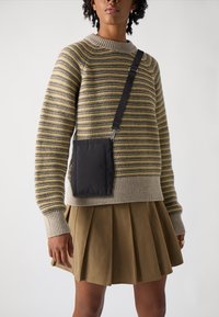 Sweter w paski, dzianinowy, w beżowych i oliwkowych odcieniach, z prążkowanym okrągłym dekoltem, zestawiony z plisowaną spódnicą w kolorze khaki oraz małą czarną torebką na pasku.