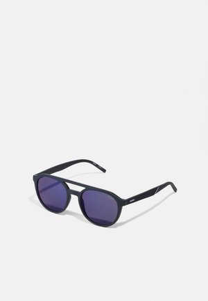 Occhiali da sole neri con lenti a gradiente viola, forma rettangolare, finitura opaca, e una stecca sottile e texturizzata con un accento bianco.