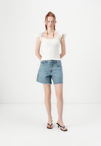 Valkoisen smockatun tanktopin, jossa on pitsireunaiset hihat, parina siniset farkkushortsit, joissa on repaleinen helma, ja mustat hihnalliset korkosaappaat.