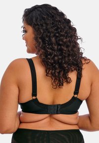 Sostenedor negro con tirantes con borde de encaje, cierre de gancho y ojo en la parte posterior, material suave y diseño sin costuras. Cabello rizado parcialmente visible.