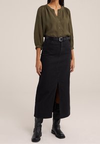 Olijfgroene blouse met knopen en lange mouwen. Zwarte denim maxi rok met een split aan de voorkant, gecombineerd met zwart leren kniehoge laarzen.