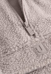 Pullover in fleece grigio chiaro con design a mezza zip, superficie testurizzata e un'etichetta logo rettangolare con una 'J' stilizzata sul davanti.