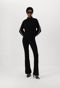 Pulover negru cu guler înalt de tip ribbed, cu accente contrastante, asortat cu pantaloni negri evazați și pantofi cu toc înalt cu vârf ascuțit. Design slim fit.