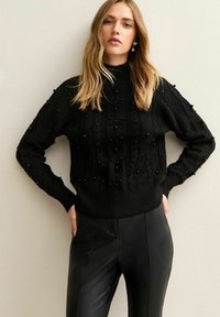 Maglione nero a maglia con dettagli in perline 3D, con collo alto e maniche lunghe. Abbinato a pantaloni neri in pelle sintetica.