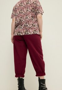 Lyhyet hihat kukkakuosisessa paidassa, viininpunaisia ja kermaisia sävyjä, yhdistettynä käännettylahkeisiin viininpunaisiin housuihin ja mustiin nauhaketjullisiin saappaisiin.