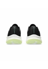 Zapatillas deportivas negras con una parte superior texturizada, suelas acolchadas blancas y sutiles acentos verdes en la marca del talón y la suela.