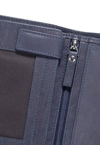 Tmavě modrá peněženka s texturovanou kůží, přihrádkou na zip a sekcí na karty. Má kontrastní prošívání a bezpečný klopový uzávěr.