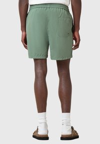 Shorts leggeri e verdi con vita elastica, tasca posteriore e texture liscia. Indossati con calze bianche e sandali marroni.