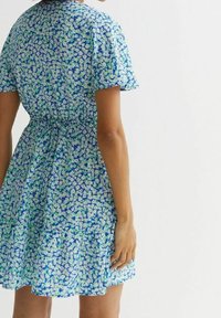 Květinové šaty v modré, zelené a bílé barvě s krátkými rukávy, na úzkém pase a se splývavou sukní. Obsahují jemný květinový vzor.