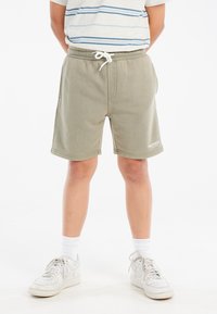 Grüne Baumwollshorts mit entspannter Passform, elastischem Bund und Kordelzug. Verfügt über Seitentaschen und Logodetail in Weiß. Kombiniert mit weißen Sneakern.
