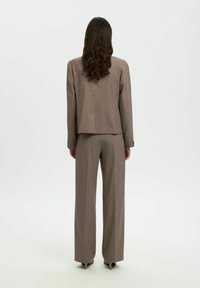 Costume marron sur mesure comprenant un blazer court et un pantalon à jambes larges en tissu structuré. Texture lisse et design minimaliste.