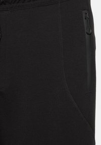 Primo piano di pantaloni in tessuto nero con tasca laterale con cerniera visibile e cuciture dettagliate lungo la cucitura.