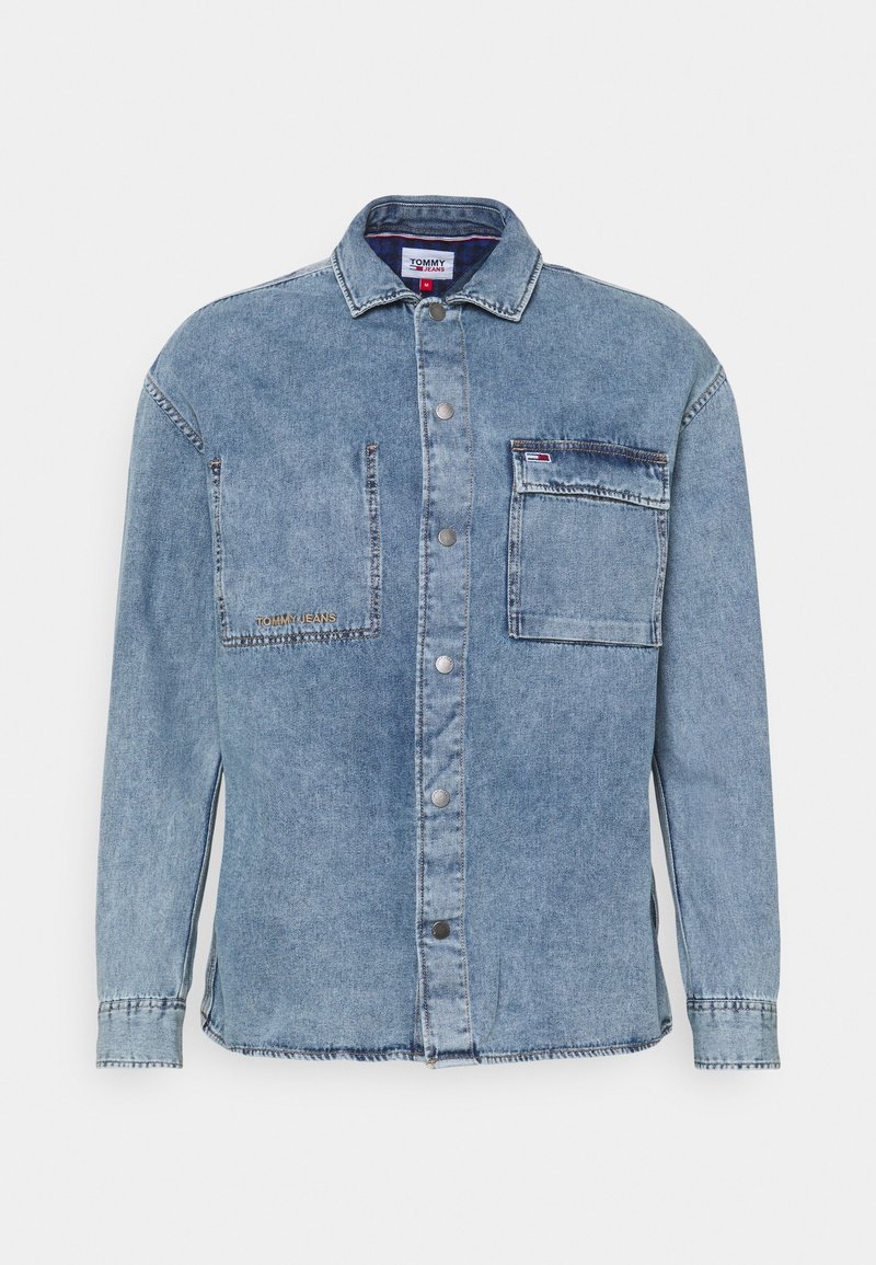 Světle modrá džínová košile na knoflíky s dvěma náprsními kapsami, jedna s klopou a malým logem Tommy Jeans, a kovovými cvočky vpředu.