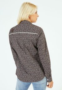 Blouse florale avec un fond marron foncé et de petites fleurs roses et blanches, présentant une ligne d'accent blanc le long du dos et des manches longues.