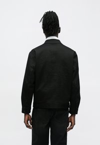 Schwarze Jeansjacke mit einem strukturierten, bestickten Pferdemotiv auf der Rückseite. Der Stoff hat eine glatte Oberfläche und eine strukturierte Passform.