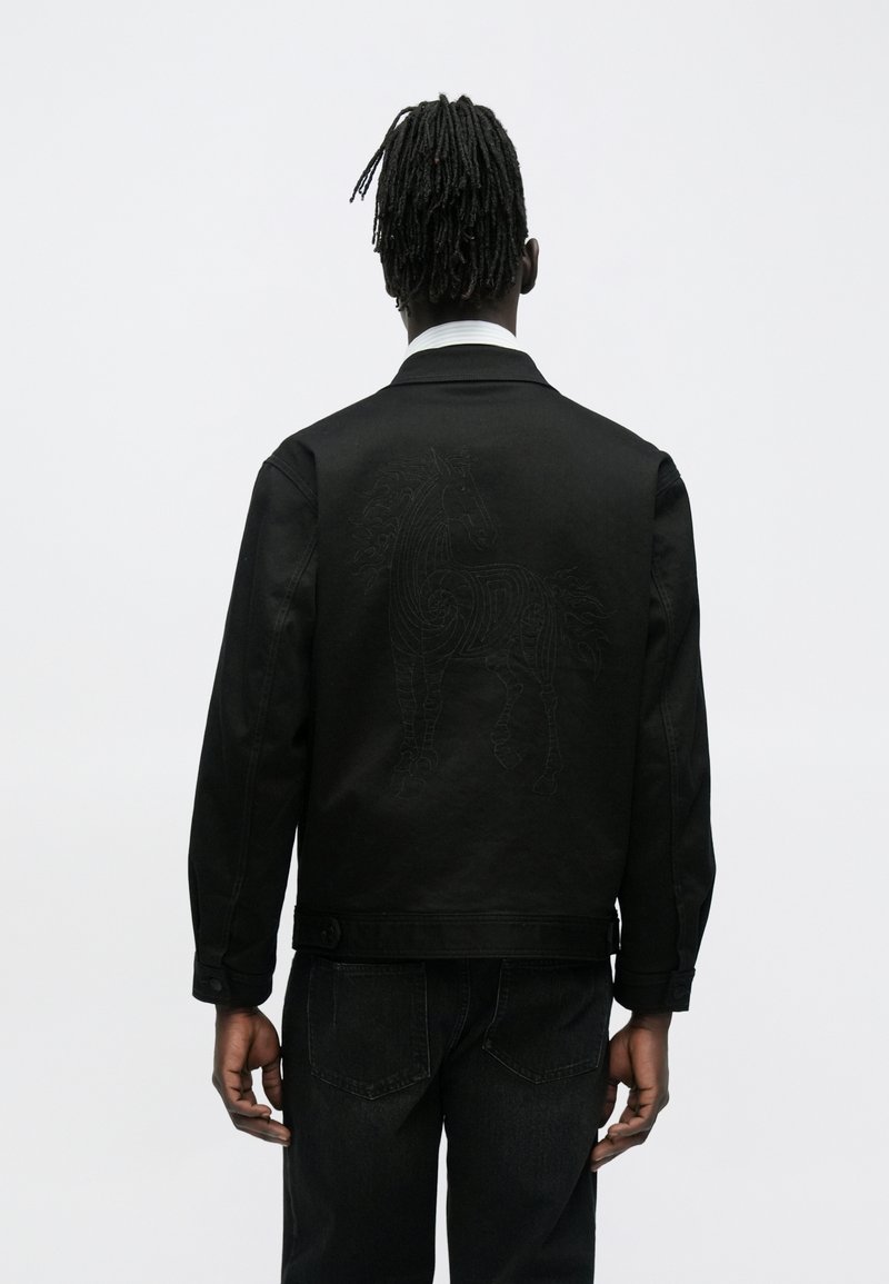 Schwarze Jeansjacke mit einem strukturierten, bestickten Pferdemotiv auf der Rückseite. Der Stoff hat eine glatte Oberfläche und eine strukturierte Passform.