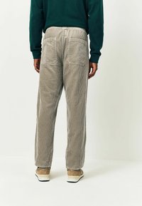 Helle graue Cordhosen mit geradem Bein, ausgestattet mit zwei Gesäßtaschen und einer strukturierten Oberfläche, kombiniert mit beigen Turnschuhen.